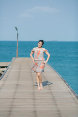 Portrait of asian woman stand and akimbo on old wooden pier over sea and blue sky background.
