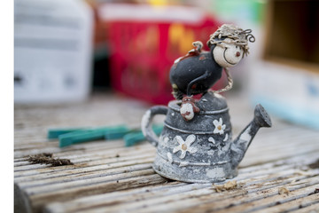 Quirky ornamental character riding on a rustic flower decorated watering can in a traditional English potting shed or green house