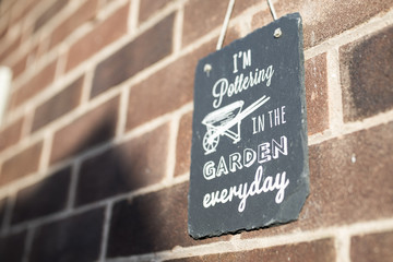 I’m pottering in the garden everyday slate garden sign against a brick wall