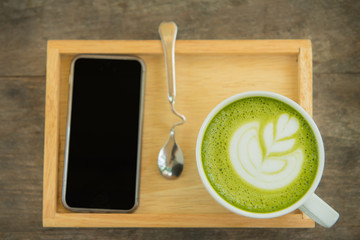 cup of green tea on wooden tray with phone  on wood table. View from the top