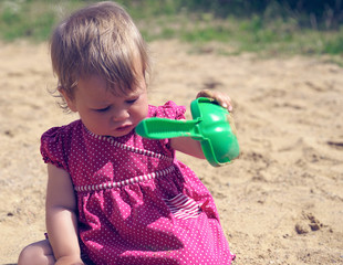 Little girl is playing with a shovel in the sandbox on a sunny summer day. The concept of education...