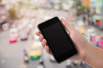 hand holding phone  on Blurred traffic jam with sunlight on street in Bangkok background.