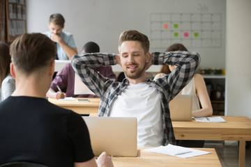 Smiling young male entrepreneur relaxing stretching back at workplace in shared office. Taking a break from heavy workflow, chilling after positive meeting, finished project, done with work concept.