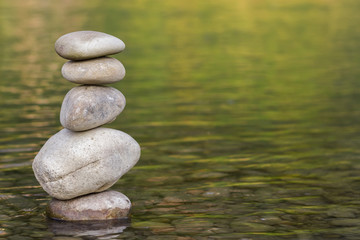 Stack of stones balancing on top in green water of the river