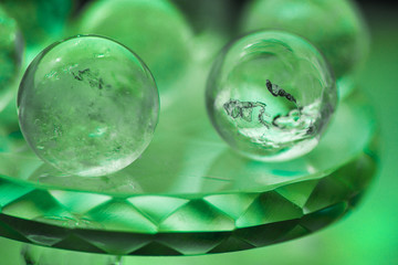 Macro shot of transparent crystal balls with colorful ornaments and sun reflections in it, on turquoise glass pad. Fortune telling. Love, money, luck, success