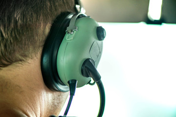 Macro shot of pilot wearing aviation headset and flying with small plane and talking with dispatcher. Ready to take off to carry passengers to another city. Flying high above clouds © lainen