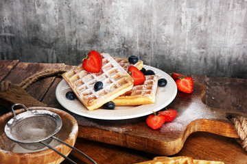 Homemade waffles with berries in plate on wooden table