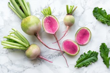 Watermelon radish (chinese daikon) with green leaves on marble table. Top view. 
