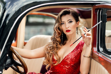 Gorgeous woman in red dress smoking in retro car
