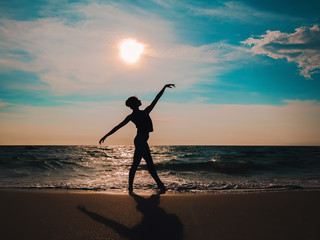 Silhouette of Young woman in casual style - denim and black top doing ballet at the beach. Attractive ballerina practices in stretching on sandy coastline in autumn. Copy space