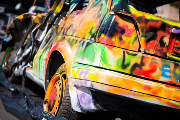 Macro shot of a colorfully painted car, an old crashed, damaged car wreck. Kids are having fun, making drawings and graffiti art, paint on wreck and tires with green, red, orange, yellow, blue colors