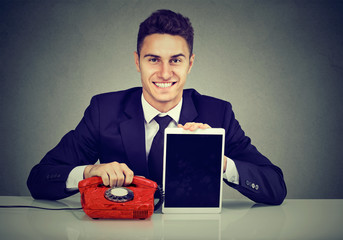 Handsome young business man sitting at desk with telephone and tablet computer