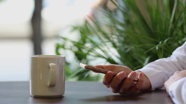 Close-up. The girl selects the necessary contact in the phone book of the mobile phone and smiles talking to the business partner.