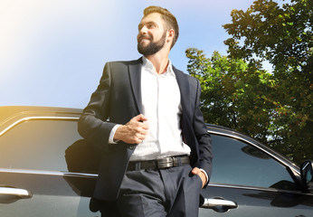 Handsome young man in elegant costume standing near car outdoors