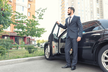 Handsome young man in elegant suit standing near car outdoors