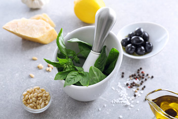 Mortar with pestle and basil leaves on table