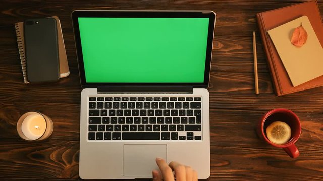 Male hands typing on the laptop computer keyboard. Green screen. Chroma key. Tea cup, notebook, candle on the vintage wooden table. Top view