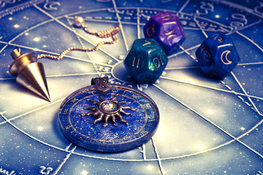 zodiac ring, pendulum, dice with astrology symbols lying on horoscope