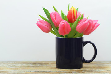 Pink tulips in navy blue mug on wooden surface with copy space
