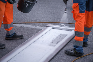 Fototapeta premium Traffic line painting. Workers are painting white street lines on pedestrian crossing. Road cones with orange and white stripes in background, standing on asphalt during road construction works