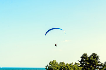 Man paragliding with blue parachute above water sea, clear sky