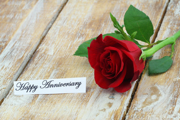 Happy Anniversary card with one red rose on rustic wooden surface
