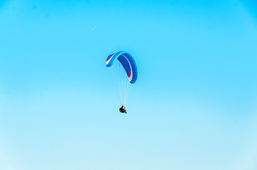Man paragliding with blue parachute above water sea, clear sky