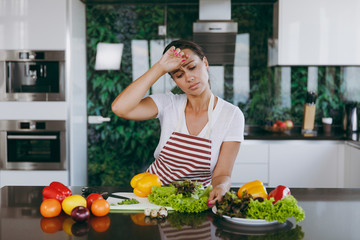 A young tired woman in apron in the kitchen. Healthy food - Vegetable salad. Diet. Dieting concept. Healthy lifestyle. Cooking at home. Prepare food