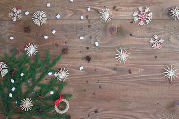 Christmas background with straw decorations, spices, marshmallow on old rustic wooden board, top view, copy space