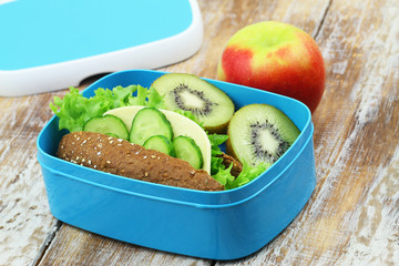Healthy packed lunch containing brown cheese sandwich, kiwi fruit and red apple on rustic wooden surface
