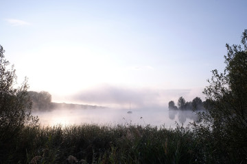 Obraz na płótnie Canvas Morning mist over lake with sailboat - 1