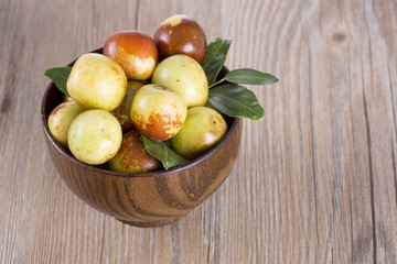 Closeup of fresh jujube fruit in a wooden bowl.