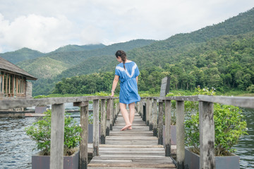 Fototapeta na wymiar Happy woman in a short dress enjoys on bridge wood with lake and mountain view
