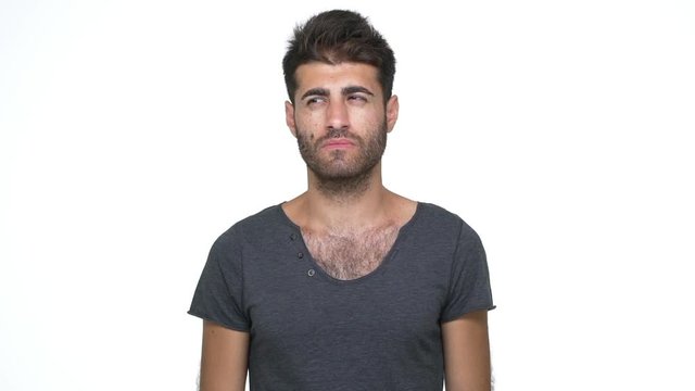 slomo young skeptical man wearing grey t-shirt looking at camera expressing misunderstanding throwing up hands saying "what" over white background. Concept of emotions