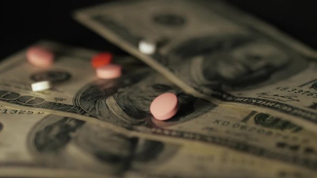Pills falling on dollar banknotes, expensive medication, pharmaceutical business. Pharmacy theme. Multicolored Pills and Capsules on money. Slow motion.