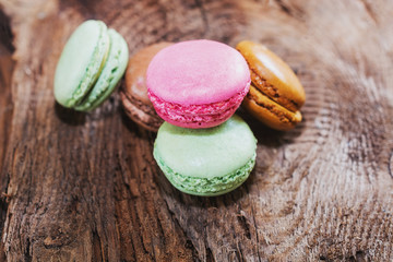 Macaroons with the flavors of coffee, pistachio, chocolate and raspberries presented on a piece of wood