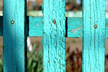 Fragment of a wooden rural fence made from painted green aged planks on the background of garden...