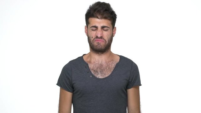 slomo skinny young man wearing grey t-shirt pinching nose with disgust on his face  due to bad smell something stinking need fresh air over white background. Concept of emotions