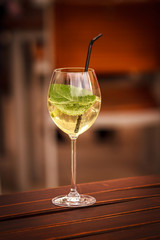 Ein Glas Hugo mit Minze und Strohhalm freigestellt auf einem Holztisch