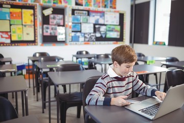 Schoolboy using laptop and mobile phone on desk