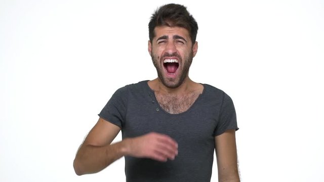 slomo picture of handsome young man in grey t-shirt looking at camera yawning covering mouth with fist stretching being sleepy over white background. Concept of emotions
