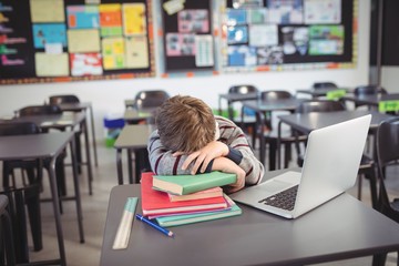 Tired schoolboy sleeping on stack of in classroom