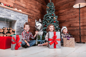 Beautiful children playing with gifts in hand in a Christmas interior with Christmas tree and fireplace. The concept of a family holiday