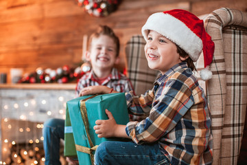 Beautiful happy laughing children play brothers with gifts in hand in a Christmas interior with a Christmas tree. The concept of a family holiday