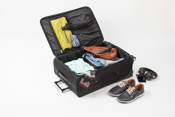 Open black suitcase with clothes, shoes, phone and headphones