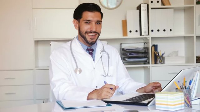 Doctor is working with documents in laptop in his work place.
