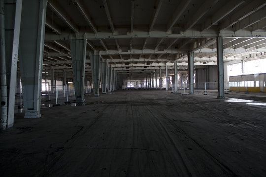verlassene Industriehalle mit grauen Stahlträgern und Fahrspuren am Fußboden