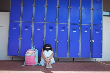 Schoolgirl sitting on pavement by lockers in corridor