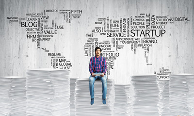 Attractive man sitting on pile of paper documents.