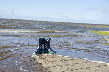 children's rubber boots stand by the banks of the sea and are being flooded